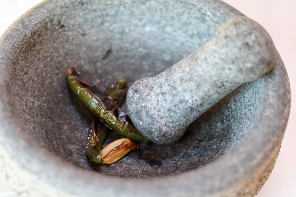 Serrano peppers chilis and roasted garlic in a mortar and pestle or molcajete. Authentic Mexican Salsa de Molcajete Recipe