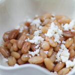 Cooked Peruvian Beans in a white bowl with cheese on top. Peruano Beans topped with crumbled cheese. Mayocoba beans with queso fresco.