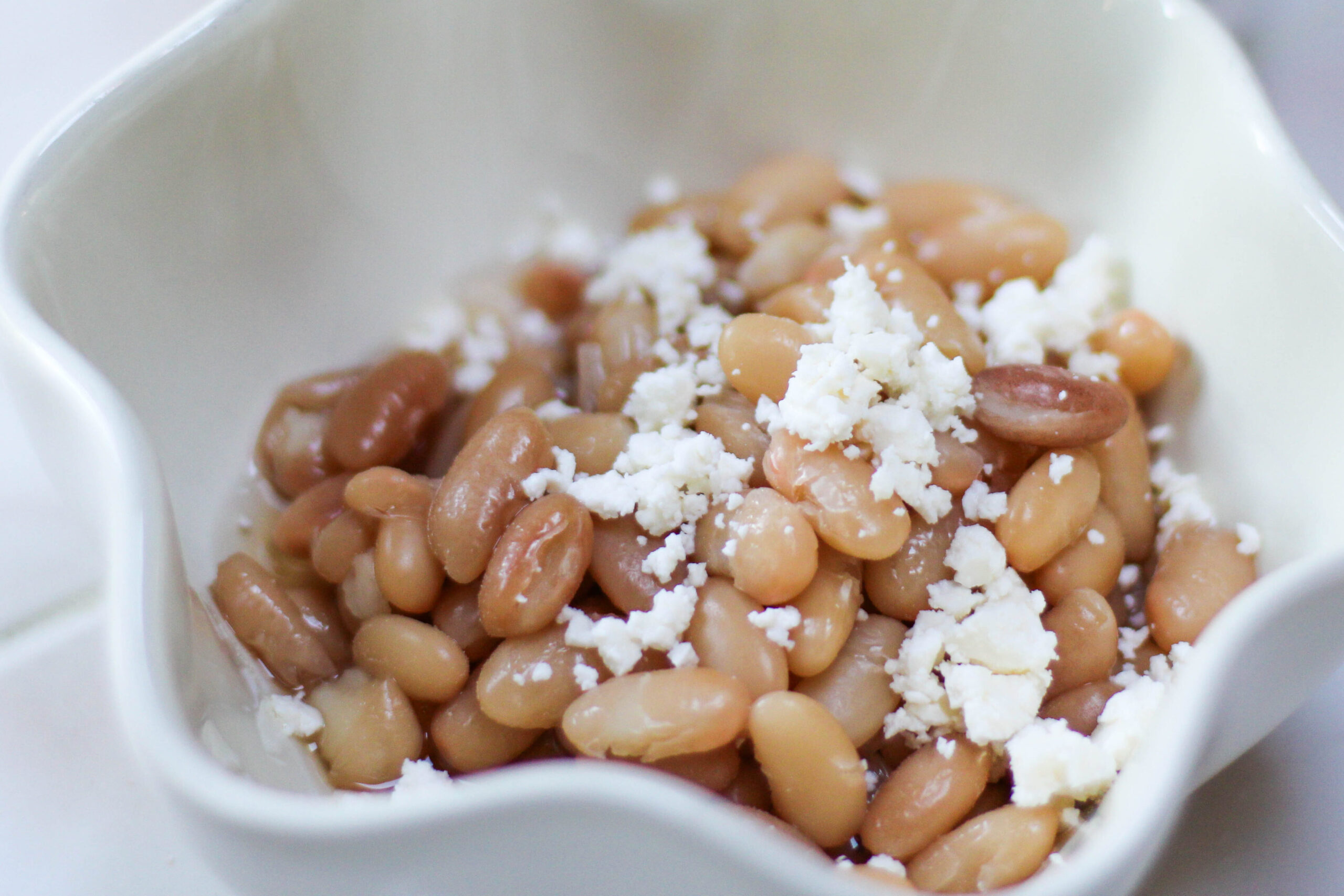 Cooked Peruvian Beans in a white bowl with cheese on top. Peruano Beans topped with crumbled cheese. Mayocoba beans with queso fresco. 