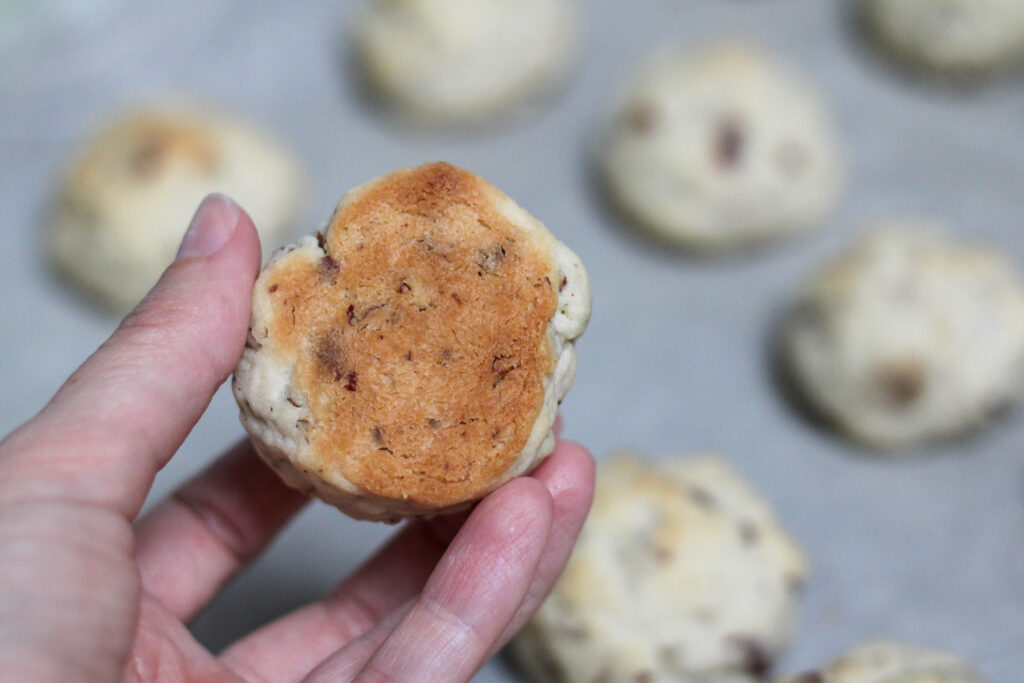 Hand showing golden brown bottom of cookie with cookies on baking sheet in the background. 