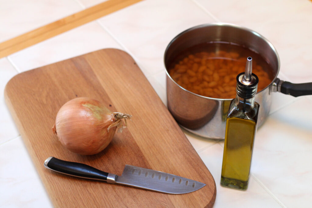 Ingredients for frijoles fritos on a white tile table including cooked beans, onion and oil.