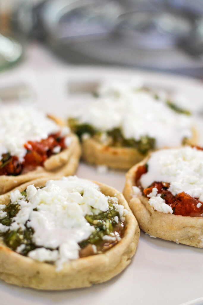 Picaditas topped with beans, salsa, crema and cheese served on a white plate. 