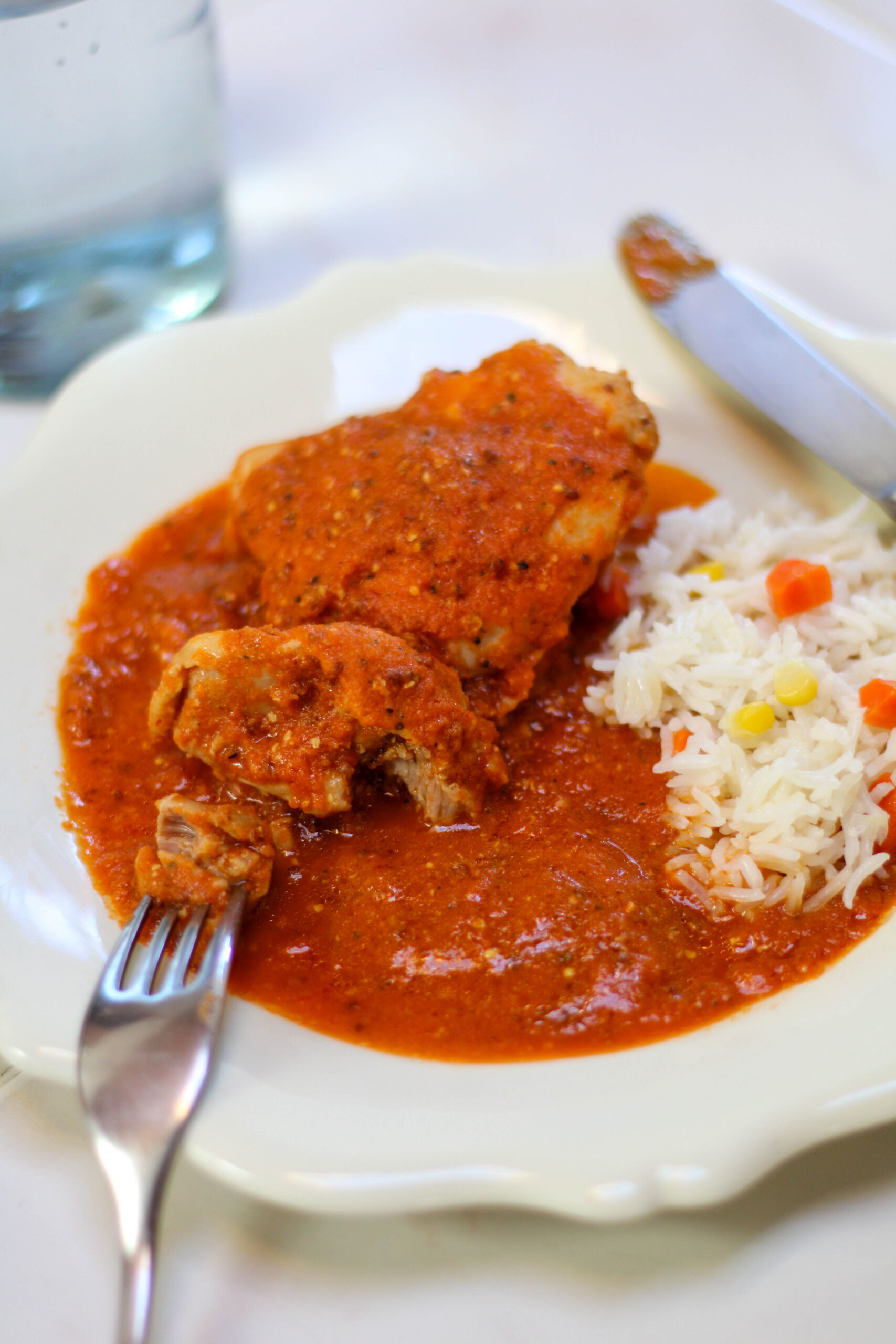 Pollo enchipotlado served on a white plate with white rice garnished with corn kernels and carrot.