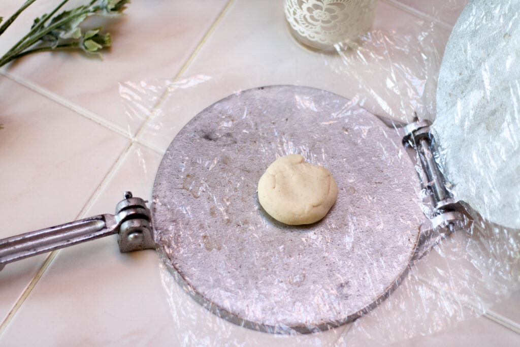Masa dough on a tortilla press lined with plastic on a white table.