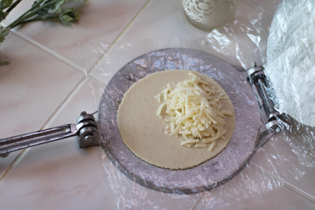 Quesadilla de Masa being made by hand on a tortilla press with shredded cheese filling.