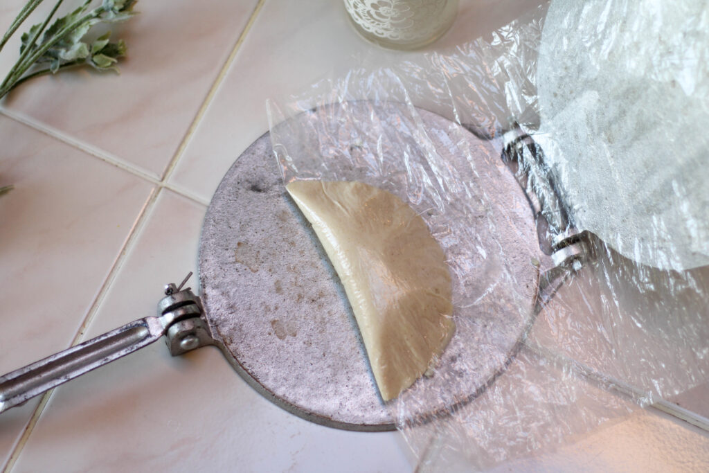 Quesadilla Mexicana made using fresh masa and tortilla press on white tile table.