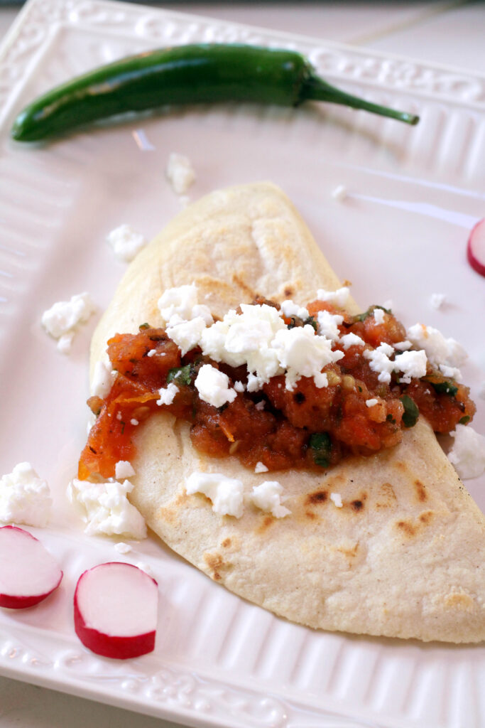 Quesadillas Mexicanas served with salsa and cheese on a white plate with radish and Serrano pepper.