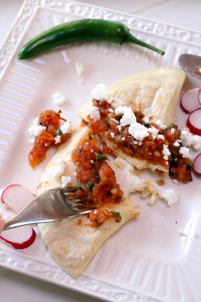Quesadillas Mexicanas topped with salsa and cheese on white plate with fork.