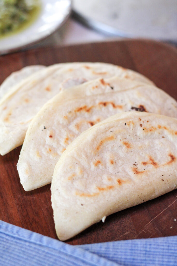 Three quesadillas Mexicanas with handmade tortillas on a dark wood cutting board with blue towel.