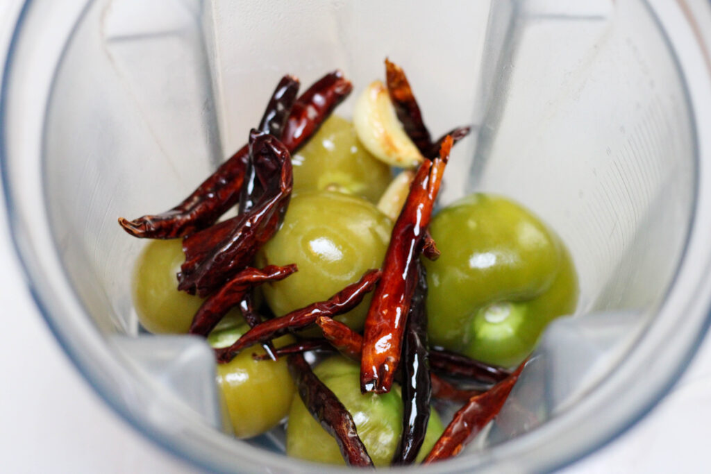 Ingredients for salsa de chile árbol in a blender including tomatillos, chile de árbol, garlic and salt. 