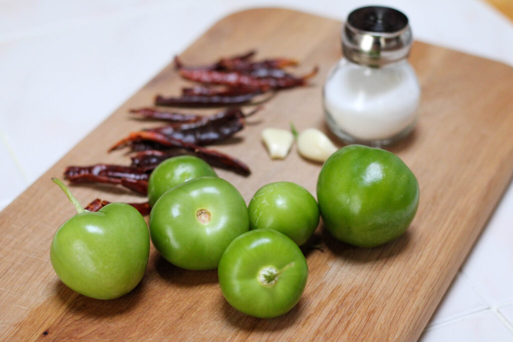 Ingredients for salsa de chile árbol on a cutting board including tomatillos, chile de árbol, garlic and salt. 