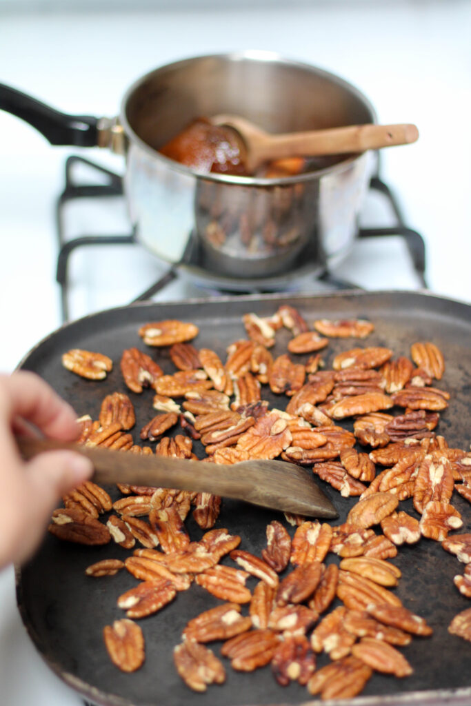 Pecans toasting on the stove with a small saucepan in the background. 