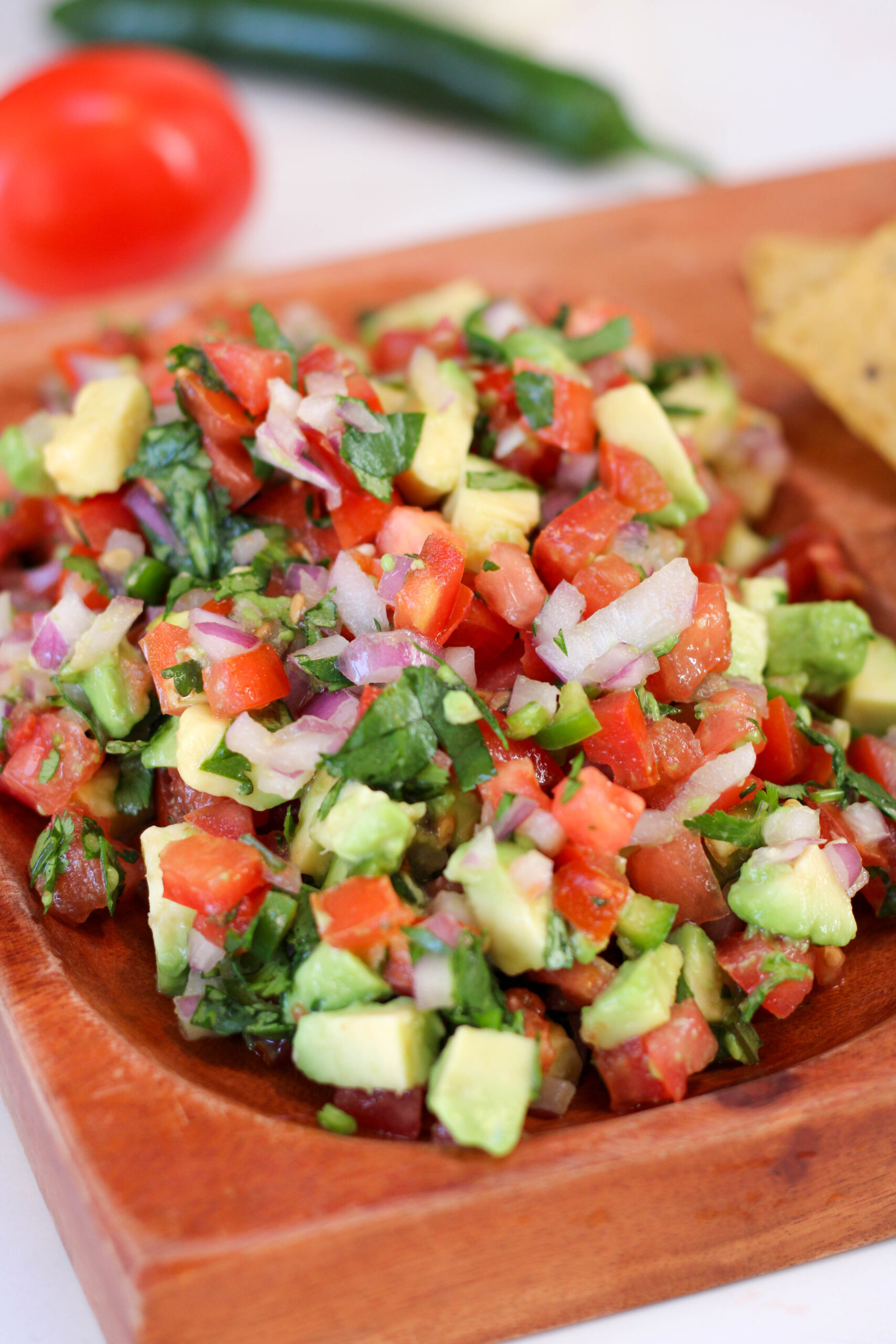 Avocado pico de gallo served on a wood platter with white background.