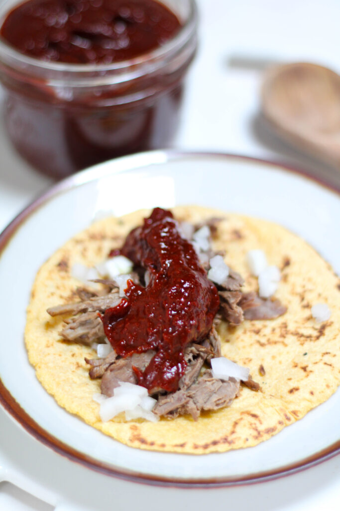 Corn tortilla taco topped with meat, onion and chile guajillo salsa. 