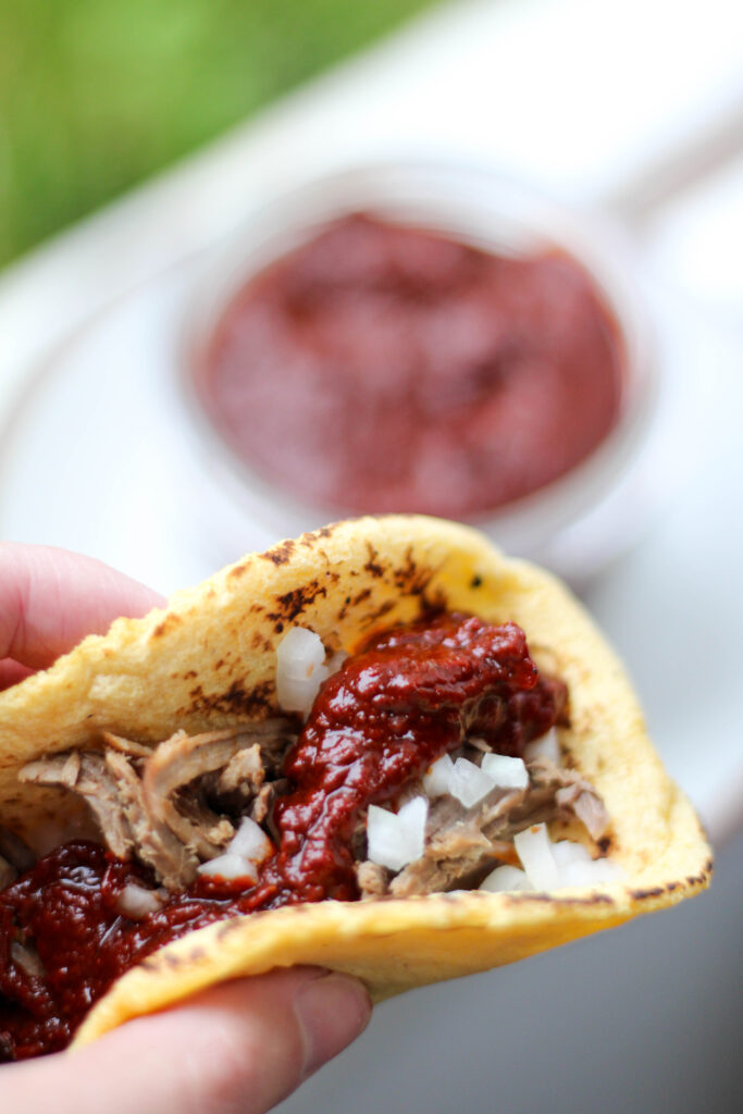 Chile guajillo salsa on a taco with corn tortilla, meat and onion. 