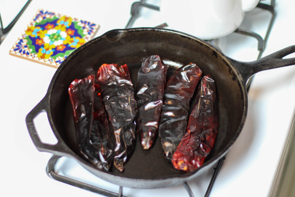 Guajillo chiles toasting in a cast iron skillet on white stove. 