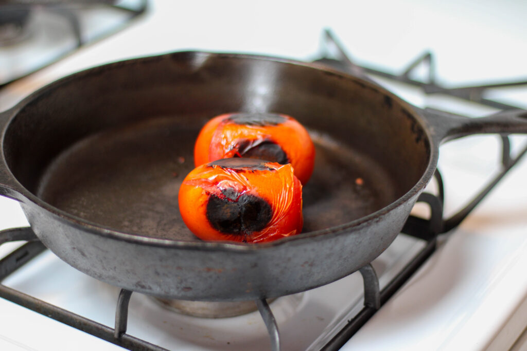 Two roma tomatoes roasting in a cast iron skillet on the stove. 