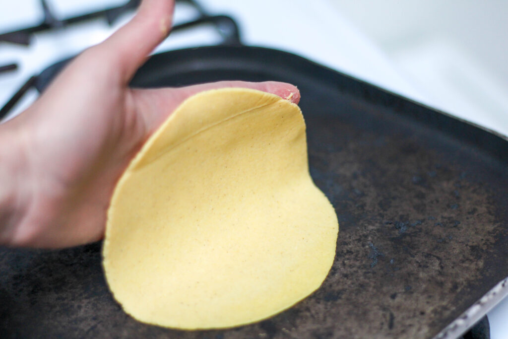 Hand placing corn tortilla on comal to cook. 