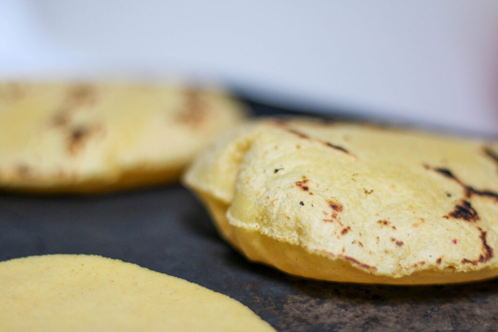 Inflated corn tortillas cooking on a comal or griddle puffed up. 