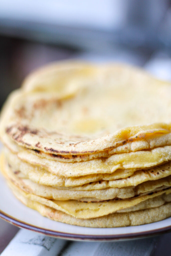 Yellow handmade corn tortillas stacked on a plate. 