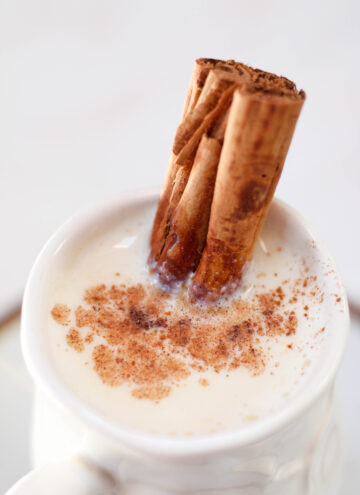Atole blanco in a white mug with cinnamon stick and ground cinnamon on top.
