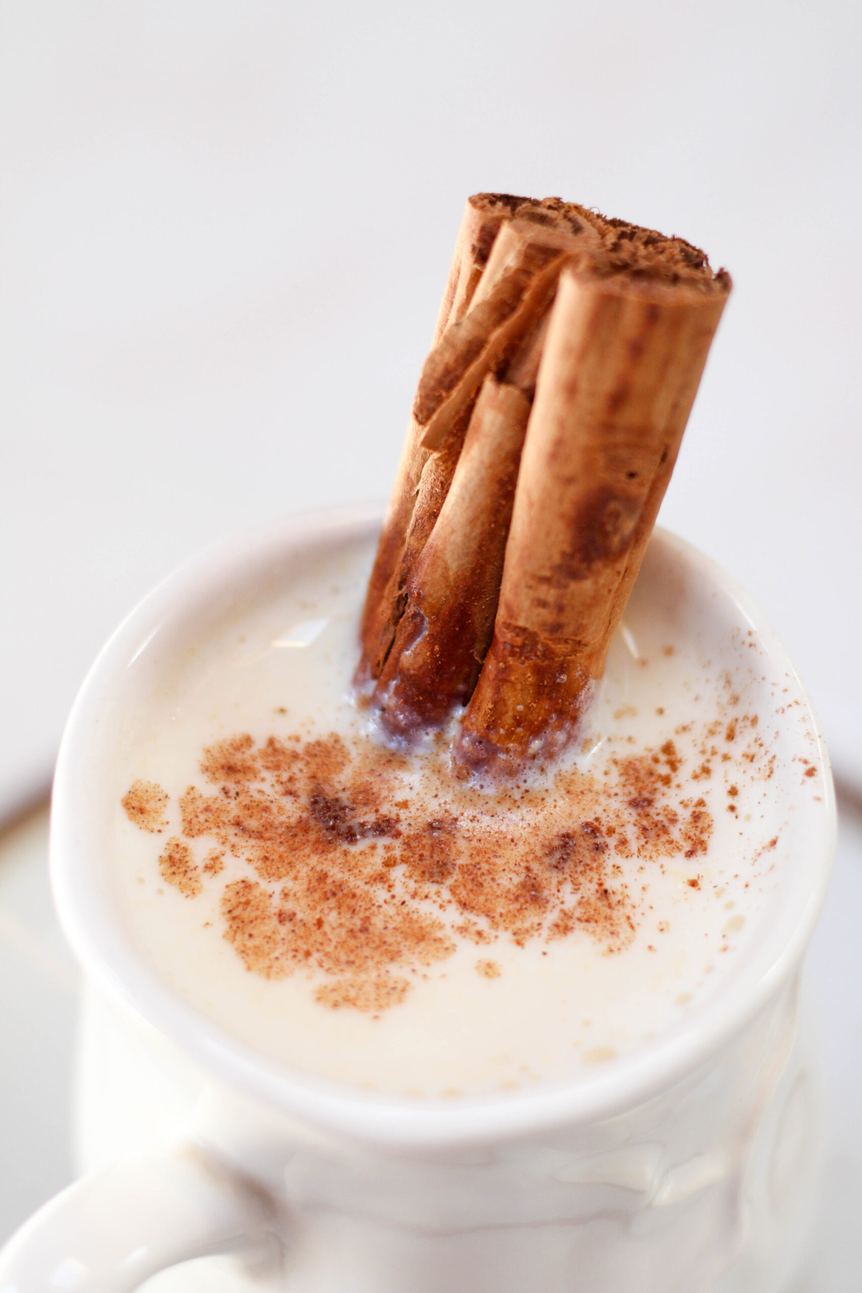 Atole blanco in a white mug with cinnamon stick and ground cinnamon on top.