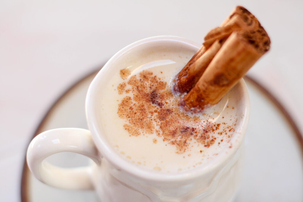 White mug full of atole blanco with cinnamon stick and powdered cinnamon on top.
