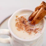 White mug full of atole blanco with cinnamon stick and powdered cinnamon on top.
