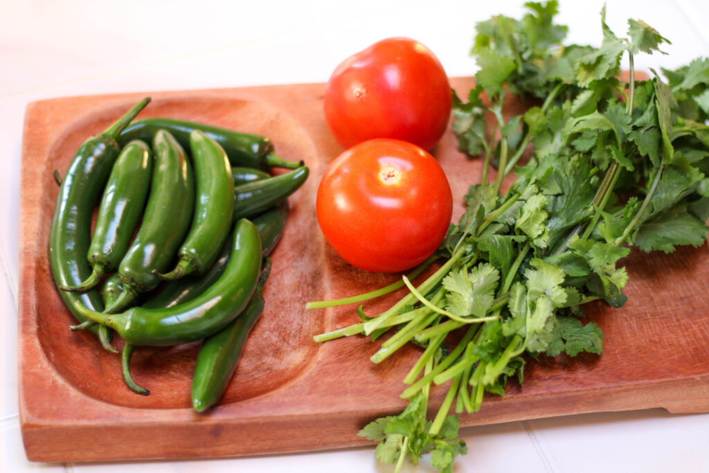 Serrano peppers, tomatoes and cilantro on a wooden cutting board. 
