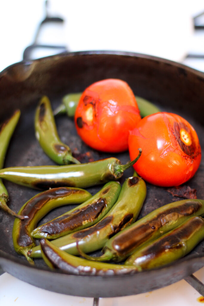 Tomatoes and serranos roasting in a cast iron skillet on the stove. 
