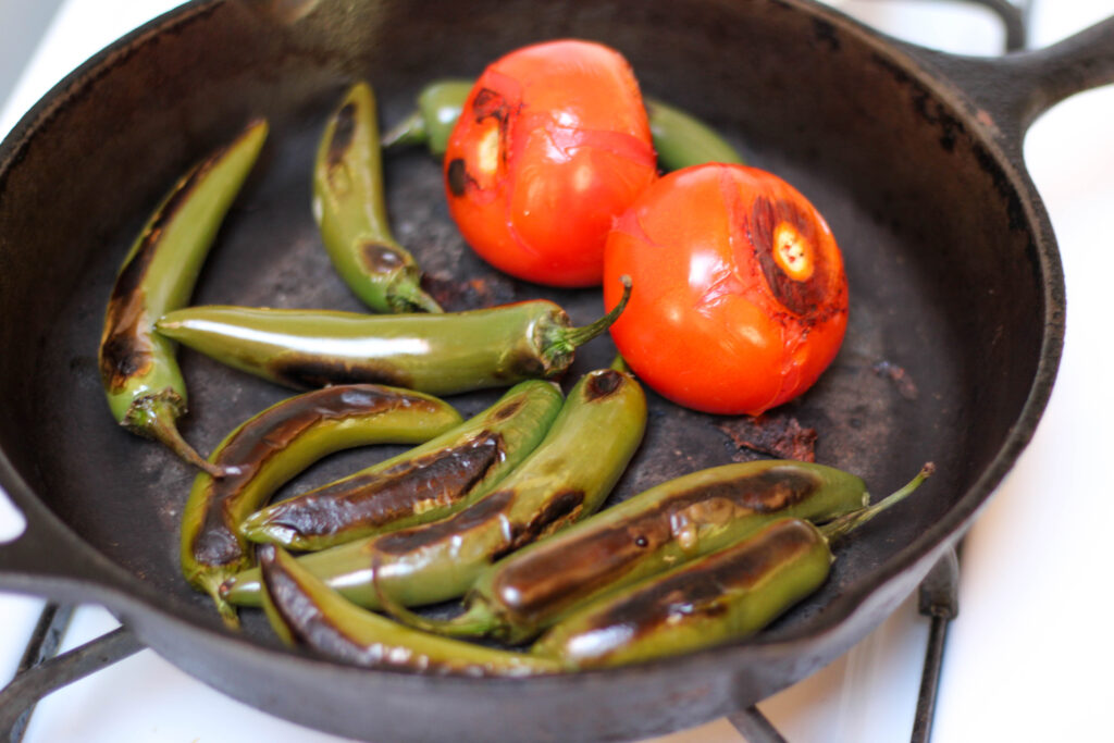 Tomatoes and serranos roasting in a cast iron skillet on the stove.