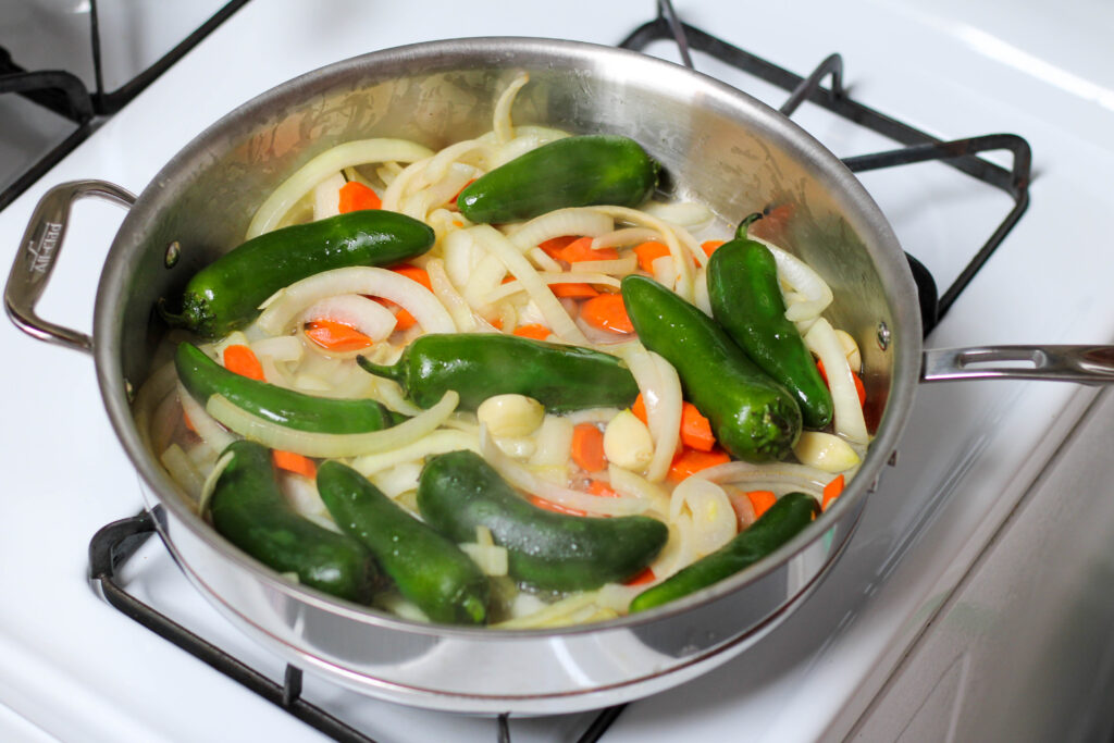 Jalepenos, onion and carrots saute in steel pan.