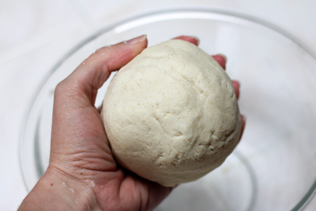 Hand holding ball of masa dough to make tetelas with a white background.
