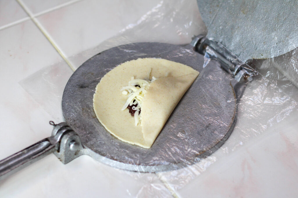 Forming a tetela with masa dough, beans and cheese on a tortilla press.
