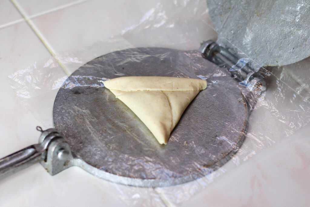 Forming a tetela with masa dough, beans and cheese on a tortilla press.