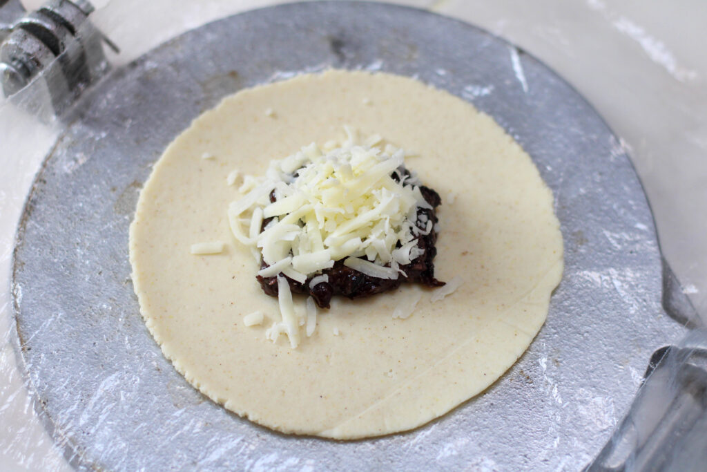 black bean and cheese filling for tetela on a silver tortilla press