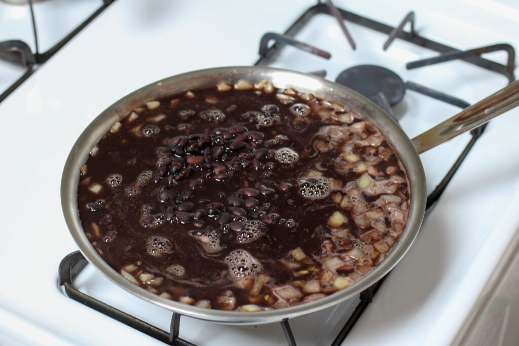 Black beans and chopped onion cooking in a large saucepan to make refried beans.