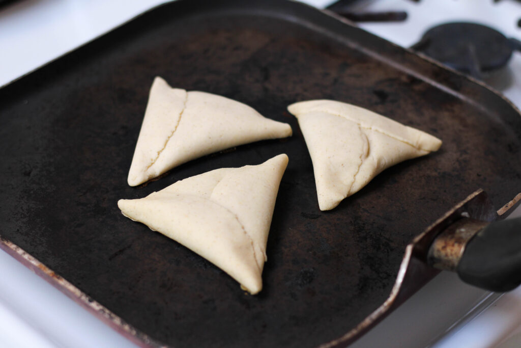 Three tetelas cooking on a comal on a white stove.