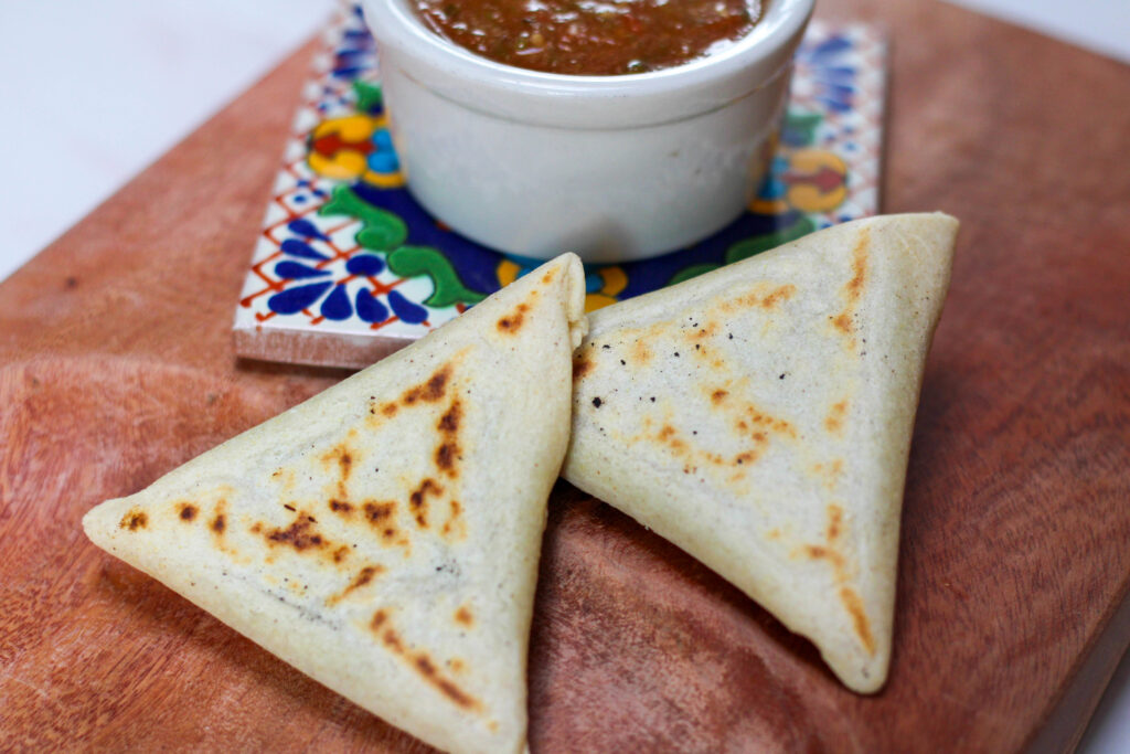 two tetelas on a wood serving dish with red salsa
