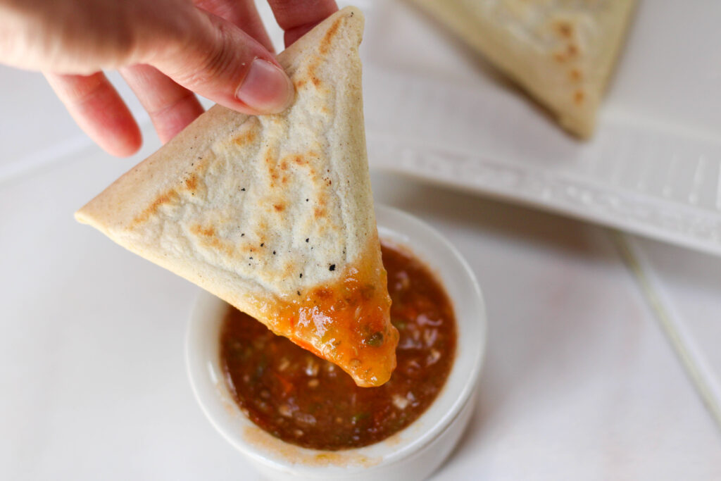 hand holding tetela and dipping it in red salsa with white background