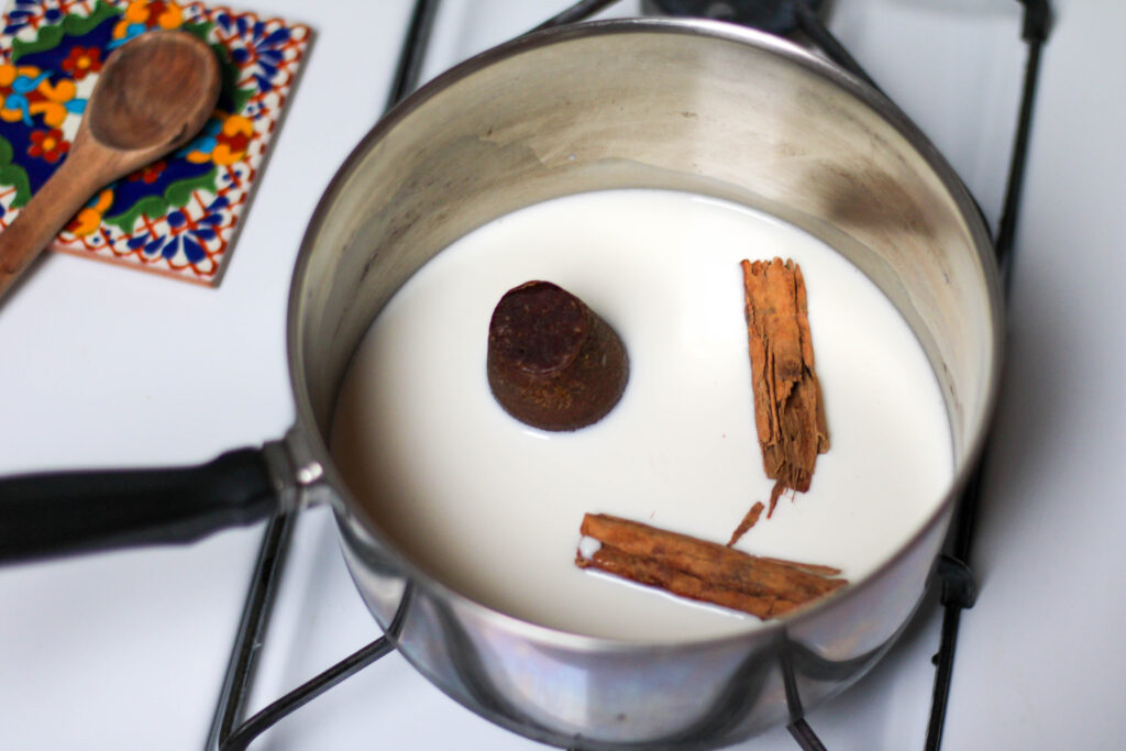 Milk, piloncillo and cinnamon stick in a saucepan over a white stove