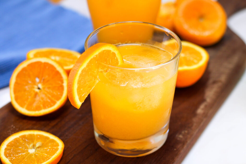 Glass of naranjada con soda with orange slices in the background