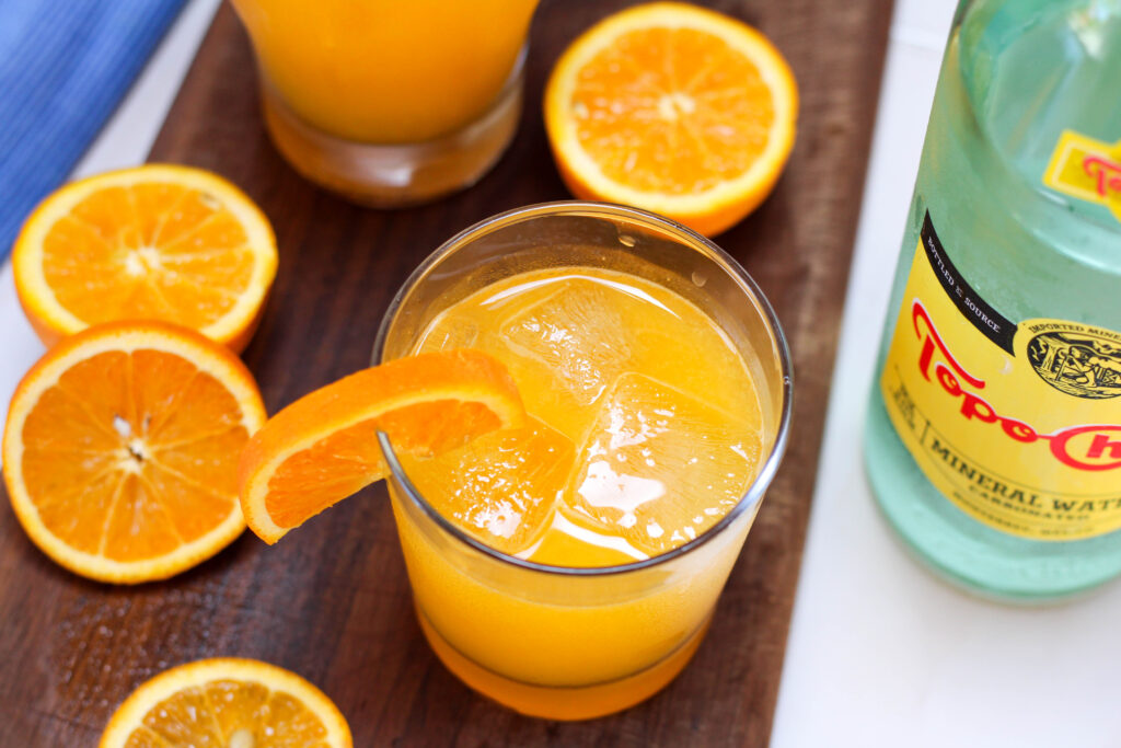 Glass of naranjada mineral with orange slices in the background