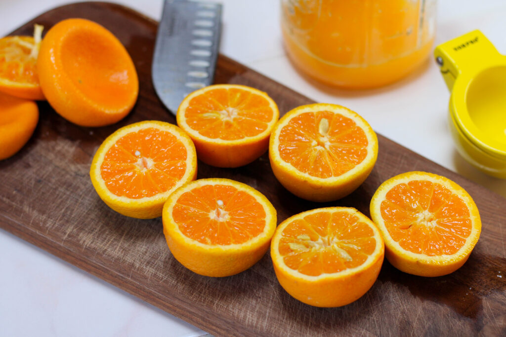 Oranges cut in half on cutting board with glass of orange juice in the background
