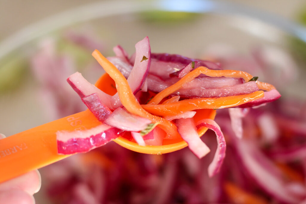 Orange spoon filled with habanero con cebolla morada or habanero with red onion
