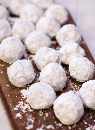 gluten free mexican wedding cookies dusted with powdered sugar on a wooden cutting board
