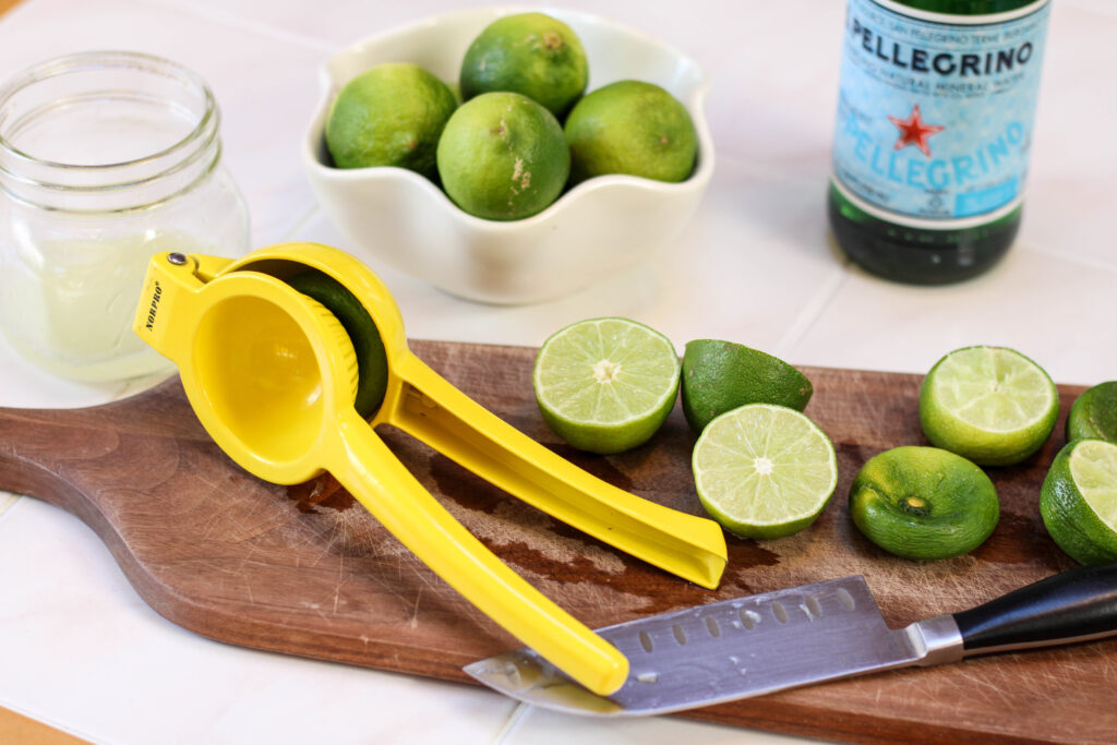 Limes and juicer on a dark cutting board with sanpellegrino in the background