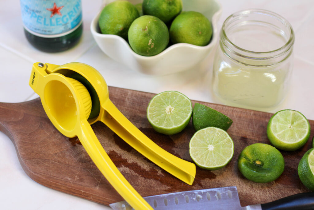 limes and lemon juicer on wooden cutting board with light background