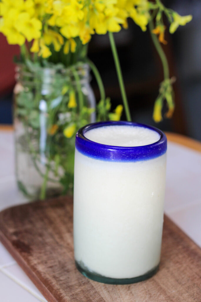 Glass of piñada on a wood cutting board with yellow flowers in the background