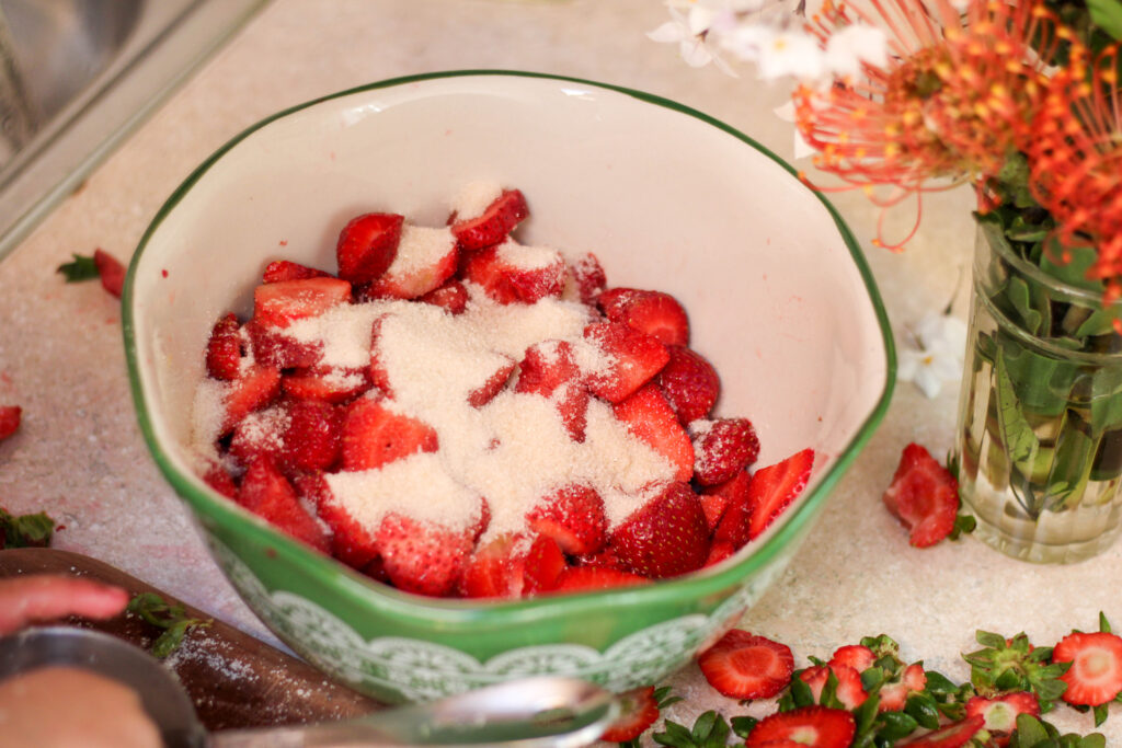 Green bowl full of sliced strawberries topped with sugar on kitchen counter
